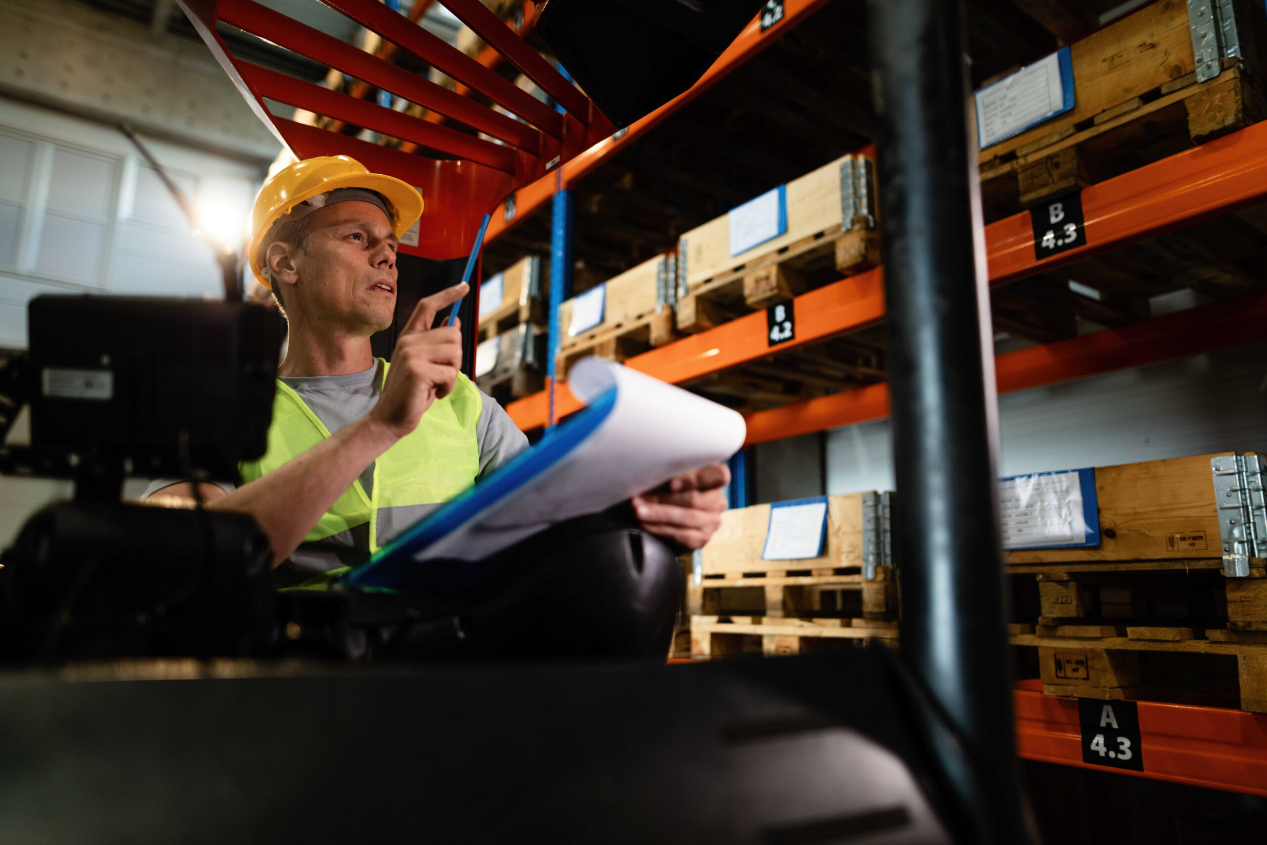 Warehouse worker in a forklift checking stock while going through paperwork.